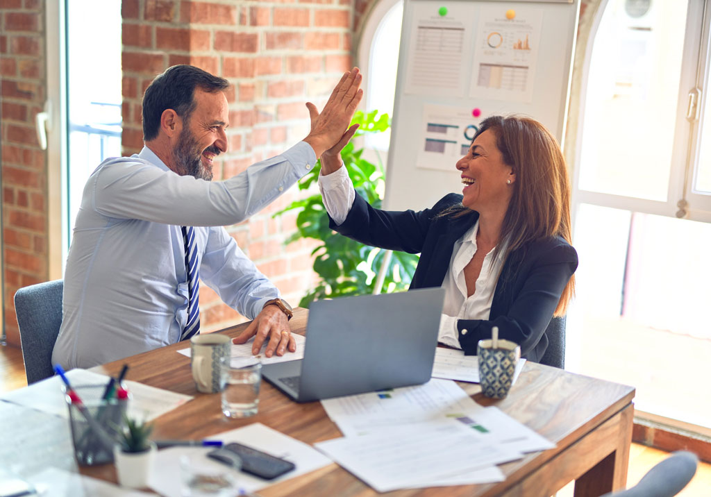 Man and woman smiling as they high-five over a business decision.